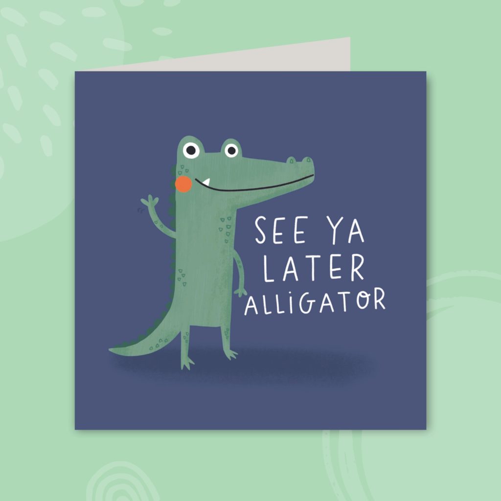 Image shows a blue greeting card on a pale green background. The card has a cute illustration of an alligator character waving and reads 