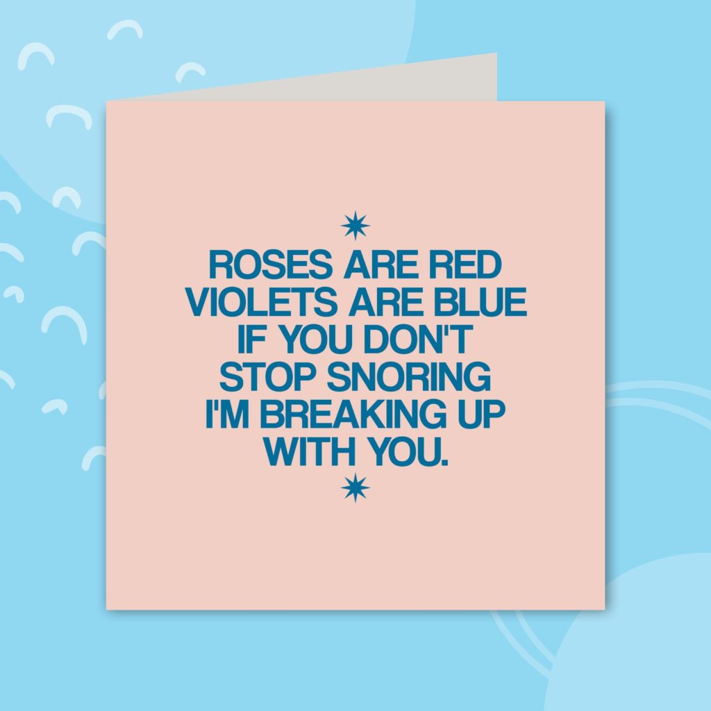 Image shows a greeting card on a sky blue background. The card is a light pink with dark blue text. The text reads 